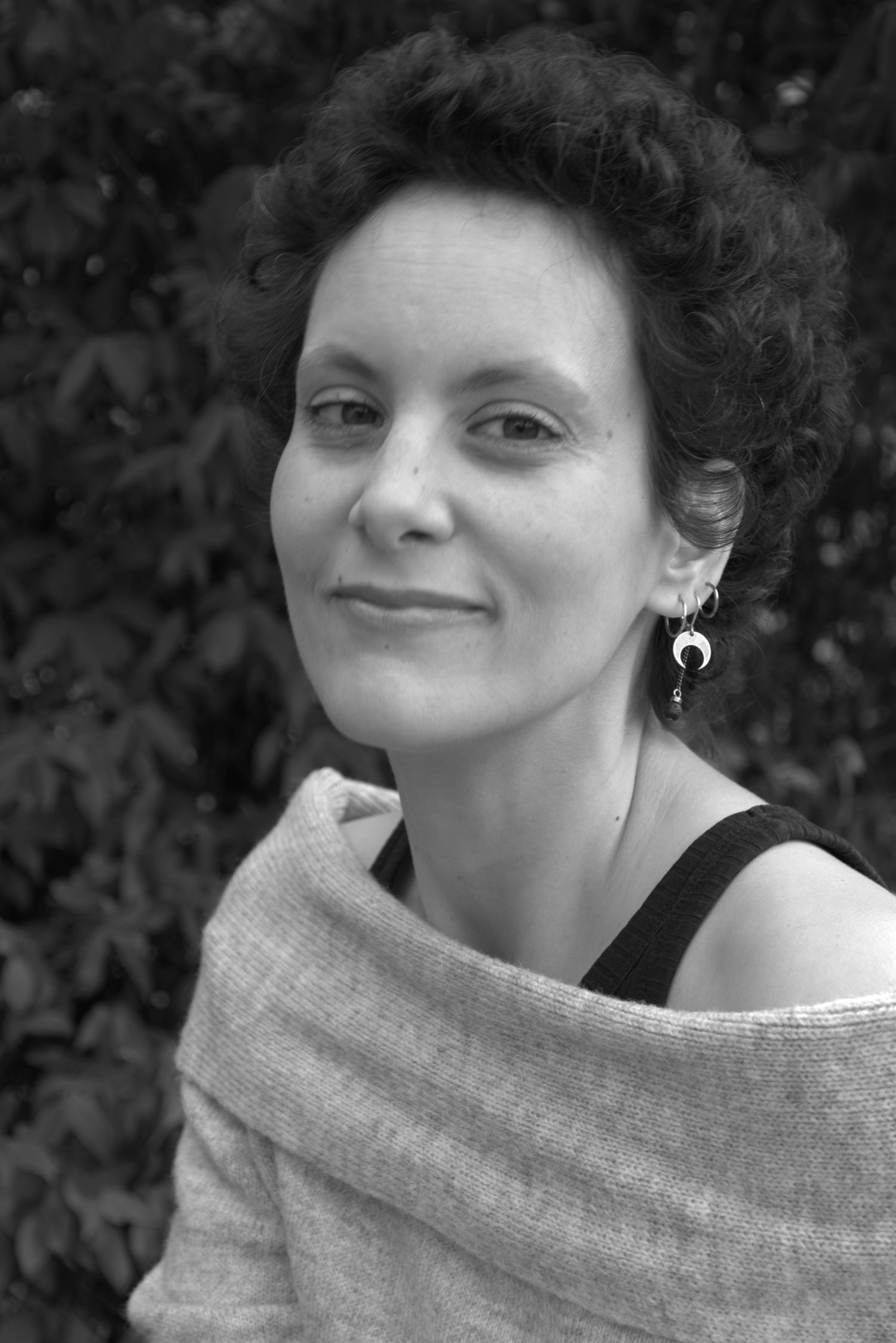 Portrait en noir et blanc de Rachel Arriaga, de trois quarts, devant un feuillage